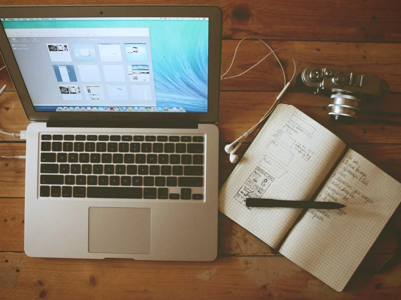 Laptop, sketchbook and camera on a wooden desk